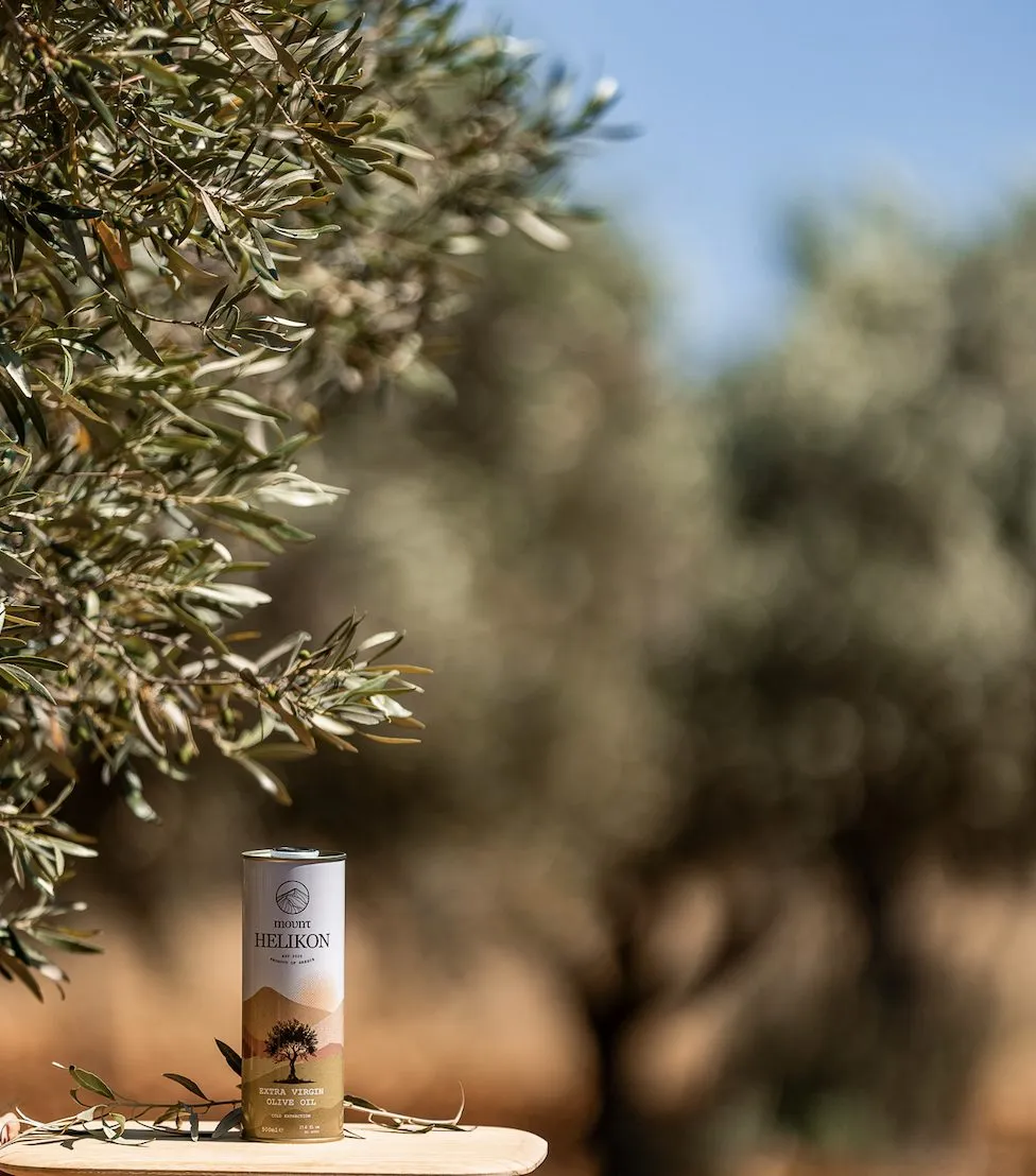 A Mount Helikon tin standing on a wooden board in the grove, under an olive branch